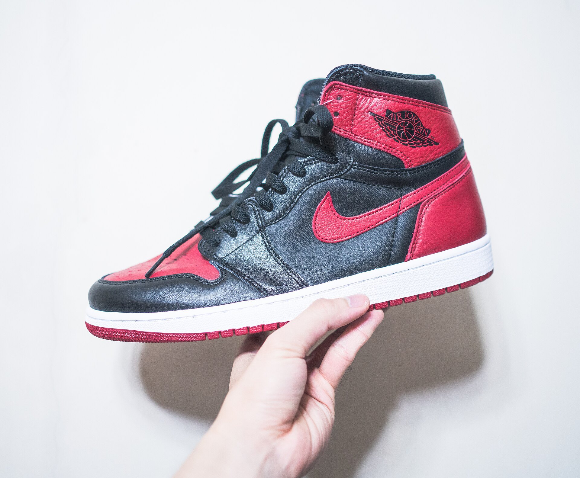 Air Jordan 1 High in Schwarz und Rot, in der Hand gehalten vor hellem Hintergrund