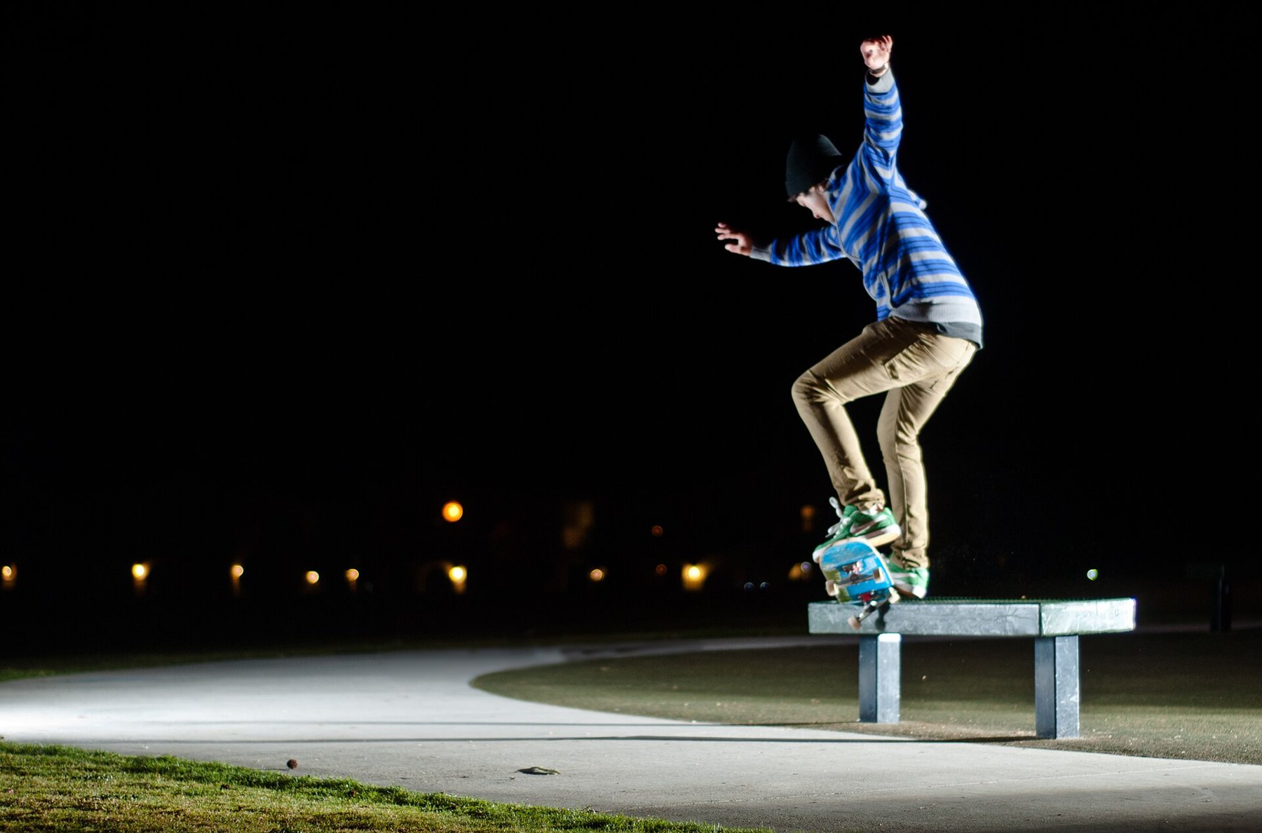 Skateboarder springt nachts mit seinem Board auf eine Bank