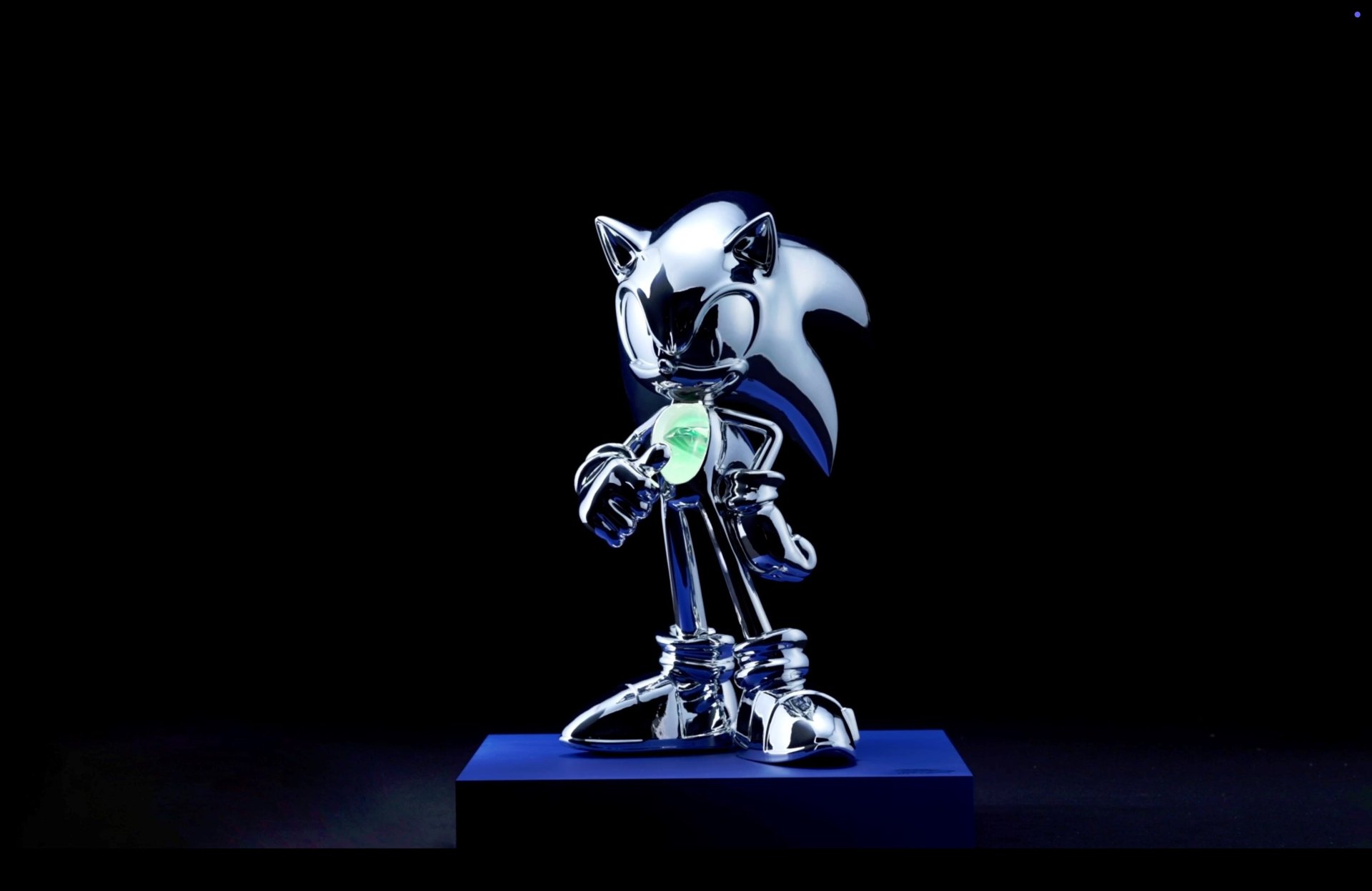 Spiegelnde Chrom-Figur von Sonic auf einem blauen Sockel vor schwarzem Hintergrund, in der Brust leuchtet ein grüner Chaos Emerald